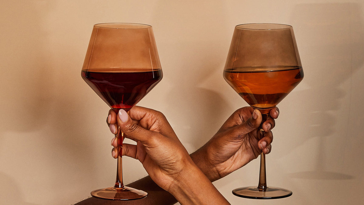 Two warm-toned wine glasses held by Black women’s hands