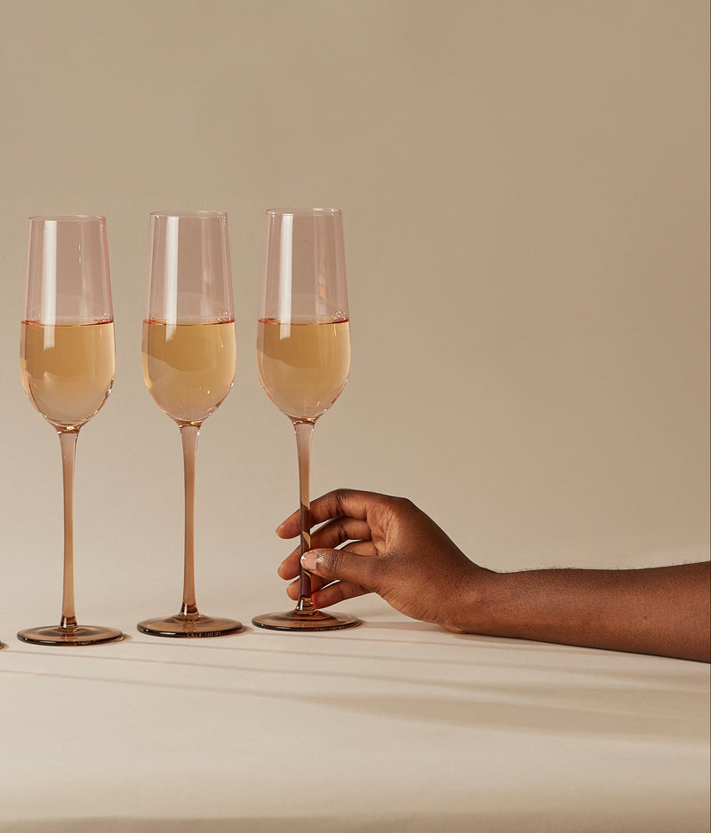 Three champagne flutes with a hand reaching toward one of the glasses