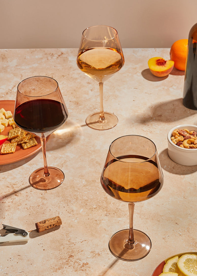 Wine glasses arranged on a table with fruit, snacks, and warm natural light